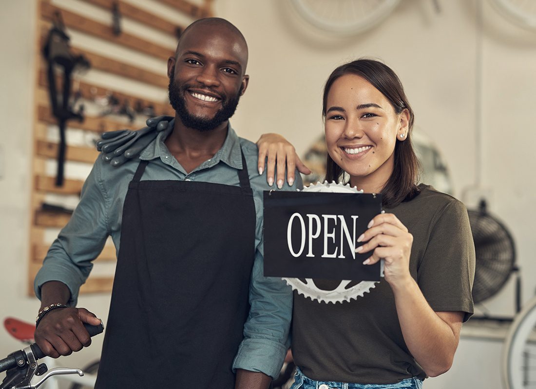 Business Insurance - Two Business Owners of a Bike Shop Hold an Open Sign