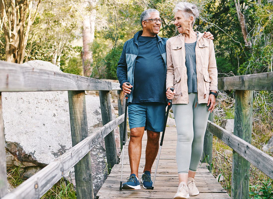 Contact - An Older Couple Taking a Hike Together Over a Small Wooden Bridge in a Forest on a Sunny Day